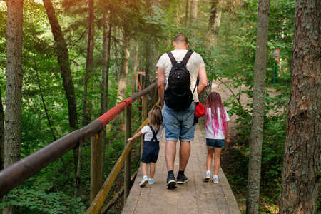 The family travels along ecological hiking trails in the forest. A girl with pink African pigtails and dreadlocks from kanekalon. A father with two daughters is walking on a wooden bridge. Family tourの写真素材
