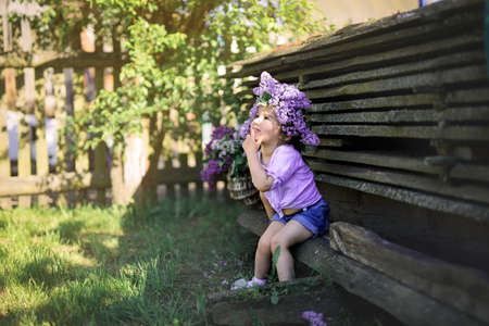 The little girl sits with a thoughtful look. The child has a wreath of lilac on his head.の写真素材