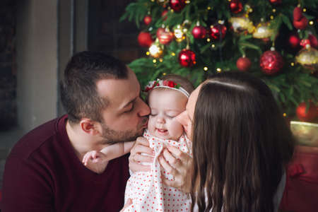 Parents kiss a little girl. A Christmas garland is shining brightly in the background.の写真素材