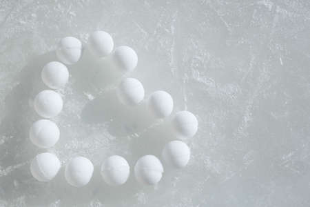 A lot of snowballs laid out on the ice in the form of a heart. Frozen ice in the scratches. copy space. Winter fun, playing with snow, children's games.の写真素材
