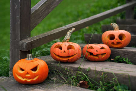 Pumpkins with carved faces and various emotions stand on the steps of an old wooden staircase near...