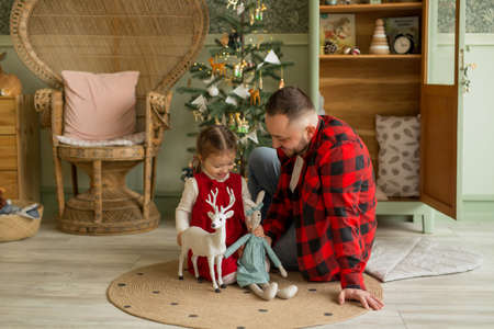 A father plays with his daughter on the floor in a children's room with Christmas decorations and a Christmas tree. Light green interior of the room. looking forward to the new year and Christmasの写真素材