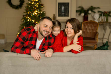 A happy girl with her parents on the eve of the new year in a room with a Christmas tree and a garland with lights. Family on christmas eveの写真素材