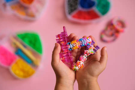 A handful of braided bracelets made of elastic rubber bands, a machine for making and a slingshot for weaving in the hands of a child. Hobbies for the development of hand motor skillsの写真素材