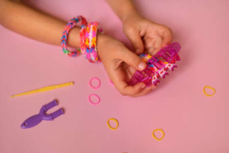 Loom for weaving toy bracelets from elastic rubber bands is held by a child in his hands. A children's hobby that develops hand motor skills. copy spaceの写真素材