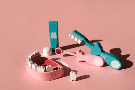 A toy model of a jaw with a fallen tooth and dental instruments and personal hygiene items of teeth and oral cavity. Toothpaste and toothbrush on pink background. Children's wooden toy. Playing Doctorの写真素材