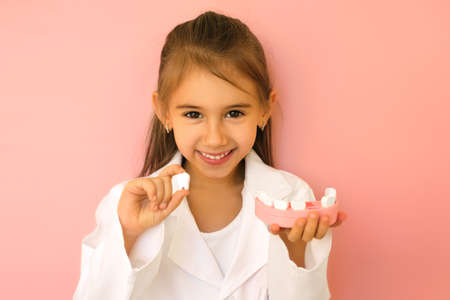 Girl in a doctor's medical on hold a jaw model with a lost tooth thin one hand and a strong white tooth in the other. Causes of loss and diseases of teeth and gums.の写真素材