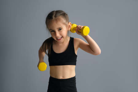 A sporty power girl with dumbbells in her hands, who is endearing to herself with her appearance, motivates her to go in for sports. Toned muscular body. Physical training. A strong, child.の写真素材
