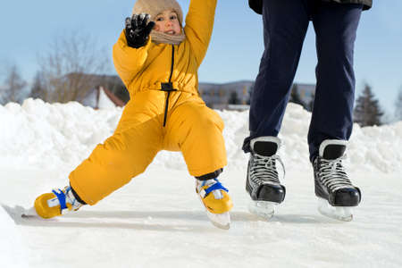 Child falls at the first attempt to get up on skates, holding father's hand. The girl is learning to...