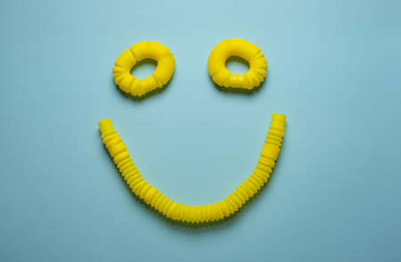 Corrugated yellow pop tubes toy are connected in the shape of a happy smile emoticon face on a blue background. Popular new modern trending toys. Playing with imagination. Positive thinkingの写真素材