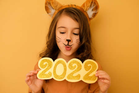 A girl with ears and tiger whiskers painted on face looks down in surprise at the numbers of 2022. The enthusiastic expression on the female face. In anticipation of the new yearの写真素材
