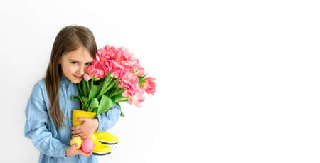 A long-haired lovely girl holds multicolored painted Easter eggs and a bouquet of pink tulips in her...