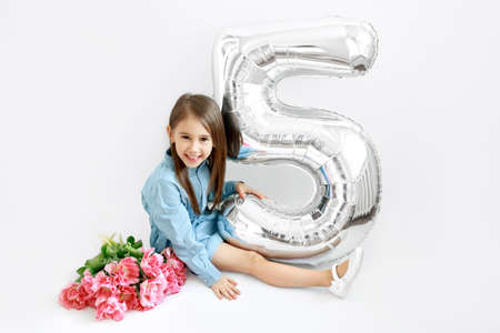 A long-haired brunette girl is sitting with a bouquet of flowers and a large balloon in the shape of...