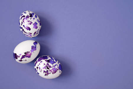 Easter eggs decorated with purple foil on a very pericolor background with copy space. white painted chicken eggsの写真素材