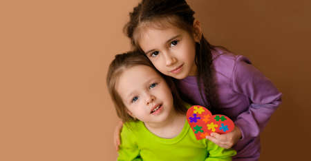 The girl embraces her sister with care and affection, holding in her hand a heart with pieces of...