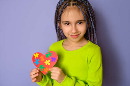 A lovely charming girl with blue Afro-pigtails holds an autism symbol in her hands as a sign of...