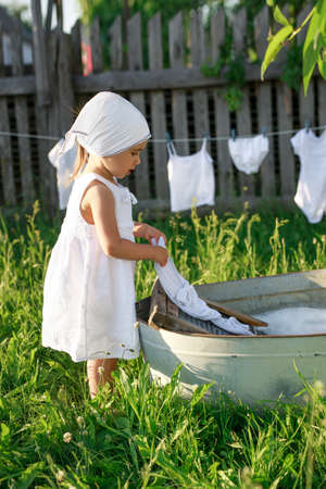 Baby washes clothes in the village in the garden in a basin on an old washing board. Bleach and detergents for white linen. Rustic retro style.の写真素材