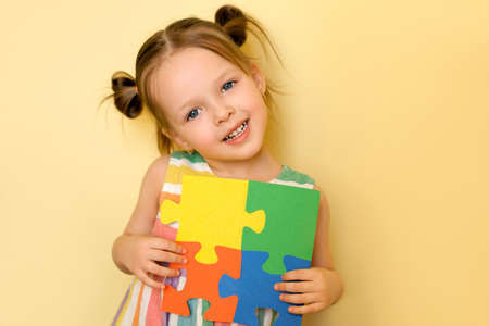 Cute pretty girl shows the pieces of puzzles put together, symbolizing unity and support for people with autism syndrome. Sweet beautiful little baby on yellow studio backgroundの写真素材