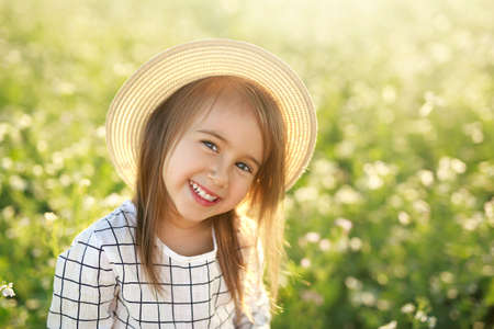 Portrait of a little cheerful laughing girl in a hat and a white checkered shirt. A baby on a background of grass and bright sun. copyspace. World Children's Day. happy kidsの写真素材