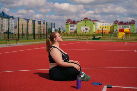 Overweight obese chubby woman doing breathing exercises in sports ground before training. Yoga pose...