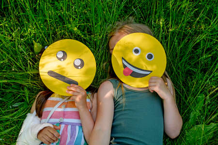 Two funny little girlfriends are lying on the lawn in the grass covering their faces with funny...