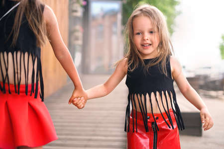 Funny shaggy unkempt girl dressed in hip hop rock style walks down a city street holding her sister's handの写真素材