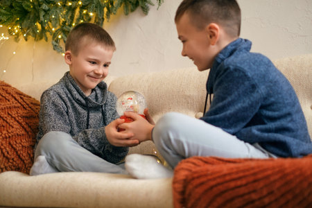 The boys are holding a Christmas snow globe with Santa Claus and flying snowflakes inside. Looking...
