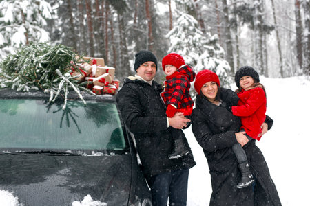 Happy parents with children in the woods by auto with a Christmas tree. Preparation for Christmas and New Year. Choosing a fir tree at a holiday fairの写真素材
