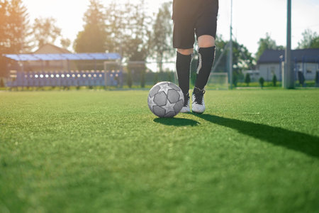 A boy in a professional uniform and cleats runs after a soccer ball making a pass on a football...