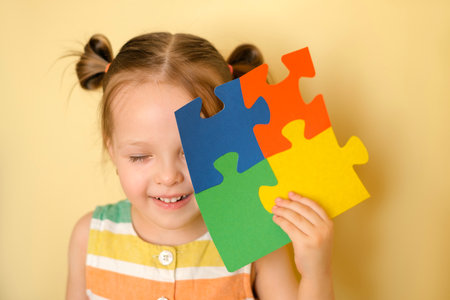 A cheerful funny girl laughs merrily with her eyes closed, holding in hand a large puzzle of colorful details - a symbol of autism as a sign of support for children suffering from the syndromeの写真素材
