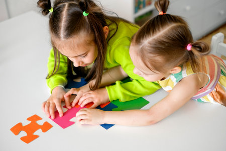 Two little girls are playing a logic game sitting at a table. preschool developmental education. Colorful puzzles are a symbol of autismの写真素材