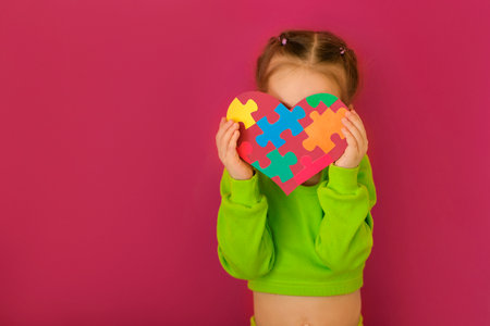 A shy lady holds a heart with puzzle pieces covering her face from embarrassment. Awareness Day about Autismの写真素材