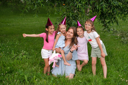 A mother of many children with four daughters is photographed in the park on the birthday of the youngest child. Girls in festive hats hug each other and laugh at the camera. mother's dayの写真素材