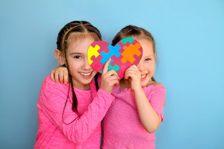 Nice cute funny little sister girls are holding a card with puzzle pieces inside - a symbol of autism. Support the unity of humanityの写真素材