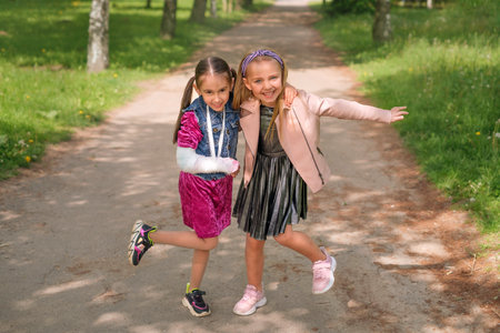 A girl with a broken wrist and a medical cast on her arm laughs merrily hugging her friend. Caring and support for loved onesの写真素材