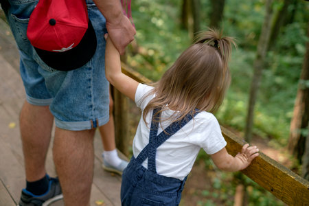 Dad holds his little daughter tightly by the hand while walking through the forests. Summer hiking on ecological trailsの写真素材