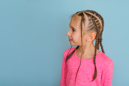A stylish girl in a pink sweater with braided pigtails with hairpins. Fashionable hairstyles of...