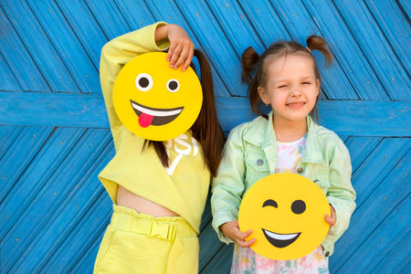 Humorous funny girls hold various funny smile faces and make faces standing at the blue wall