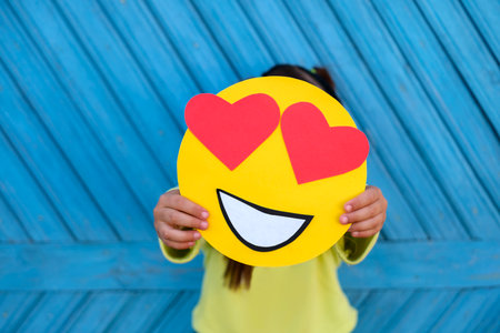 A human holds a romantic emoticon in love with eyes in the shape of hearts on a blue backgroundの写真素材