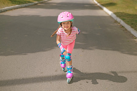 A child in sports protective gear and a helmet rushes along an asphalt track on roller skates at speed in motionの写真素材