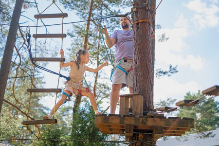 A brave girl goes through a suspended rope track with her father. Rope town at a height between the...