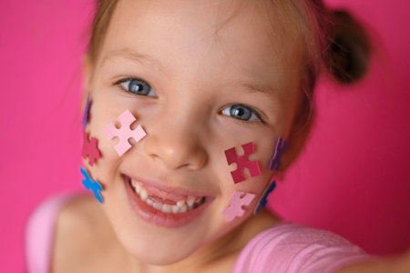 Cheerful Jolly child decorated his cheeks with multicolored puzzle pieces and takes selfies on autism Day, supporting people with the syndrome.の写真素材