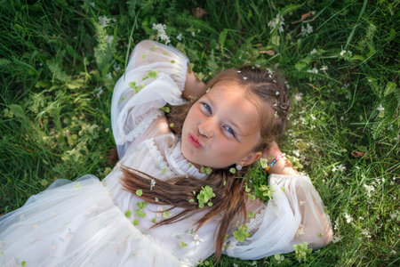 A curly-haired girl in a white fluffy dress lies on the grass, strewn with green hydrangea flowersの写真素材