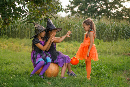 Children in witch costumes enchant a girl dressed up as a pumpkin with a bucket for Halloween sweetsの写真素材