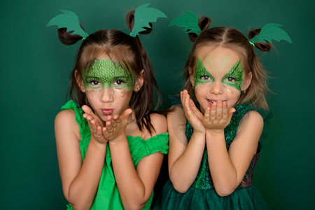 Children in the guise of a dragon - the symbol of 2024, I'm blowing kisses. Girls in green outfits on a studio backgroundの写真素材