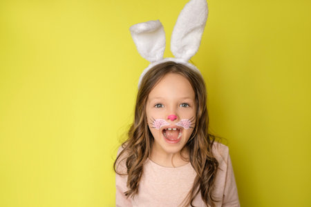 A surprised charming girl with curly hair, ears on head and a painted face in the guise of an Easter bunnyの写真素材