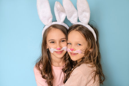 Cute cute girls with painted rabbit faces on their faces and bunny ears on heads are hugging each other and looking sweetly at the camera. Easter Holidayの写真素材