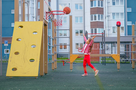 A girl on the playground makes a well-aimed throw with a basketball into a basketball hoopの写真素材