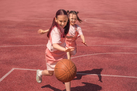 The girls are playing basketball on the sports court. The child is leading the ball. Active outdoor games for childrenの写真素材