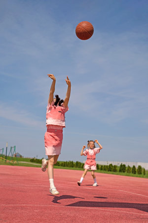 Girls on the sports court playing basketball on a sunny hot day. Active children's games on summer holidaysの写真素材
